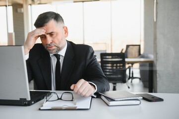 Tired stressed office worker sitting at desk and thinking, he is rubbing his eyes and feeling exhausted.