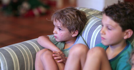 Siblings watching TV screen in night-time on sofa