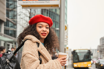 waist up portrait of beautiful curly lady in glasses holding cup of coffee and looking camera with s