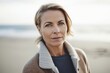 Photography in the style of pensive portraiture of a pleased woman in her 40s wearing a chic cardigan against a beach background. Generative AI