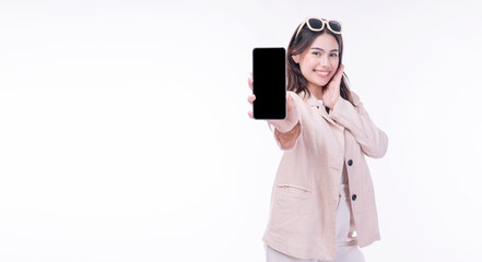 Cheerful excited young woman sunglasses showing mobile phone empty screen standing on isolated white background. Businesswomen wear suit holding smartphone looking camera. Technology app on cellphone.