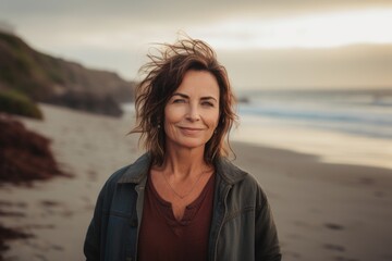 Wall Mural - Portrait of a beautiful mature woman standing on the beach at sunset