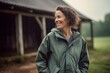 © Leon Waltz - Full-length portrait photography of a cheerful woman in her 40s wearing a lightweight windbreaker against a rustic barn or farm background. Generative AI