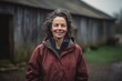 © Leon Waltz - Full-length portrait photography of a cheerful woman in her 40s wearing a lightweight windbreaker against a rustic barn or farm background. Generative AI