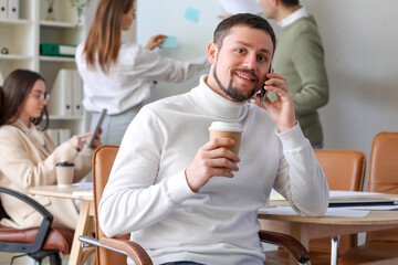 Sticker - Handsome businessman with cup of coffee talking by mobile phone in office