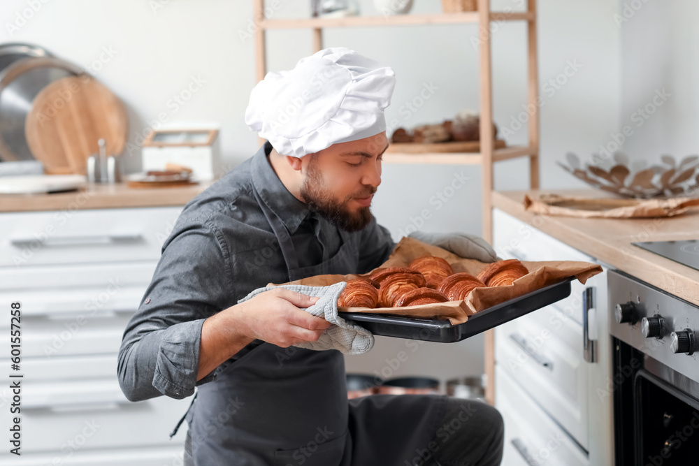 Male baker taking tray with croissants from oven in kitchen