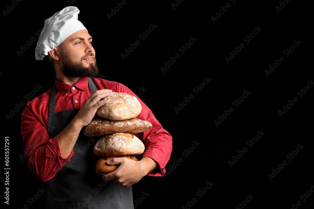 Male baker with loaves of fresh bread on dark background