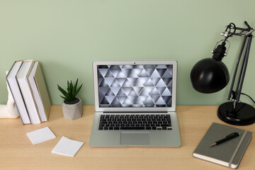 Poster - Modern laptop, books, lamp and stationery on wooden desk near green wall. Home office