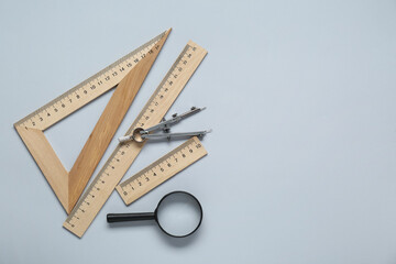 Wall Mural - Different rulers, magnifying glass and compass on light grey background, flat lay. Space for text