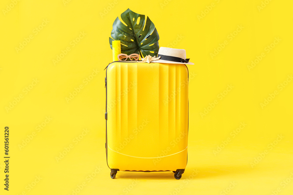 Suitcase with beach accessories and palm leaf on yellow background