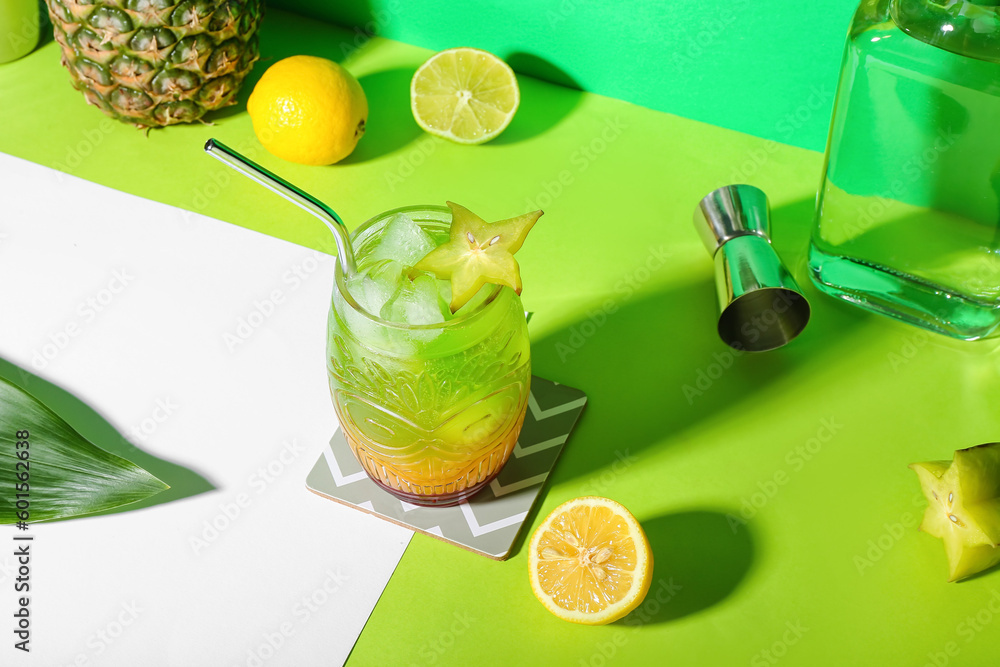 Fresh summer cocktail with carambola and straw on green table
