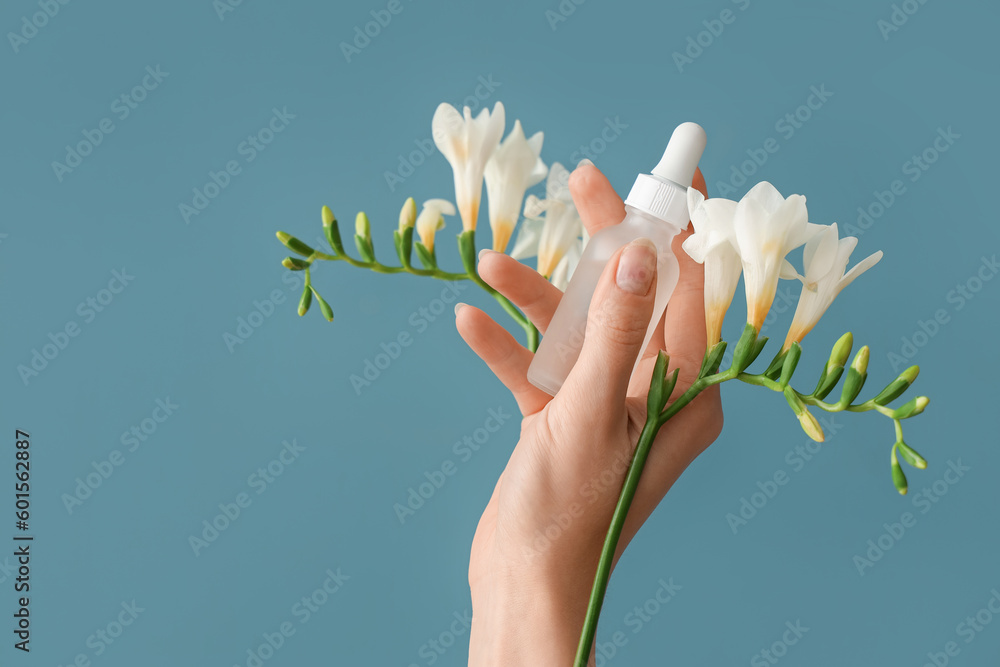 Hand holding bottle with cosmetic serum and flowers on blue background