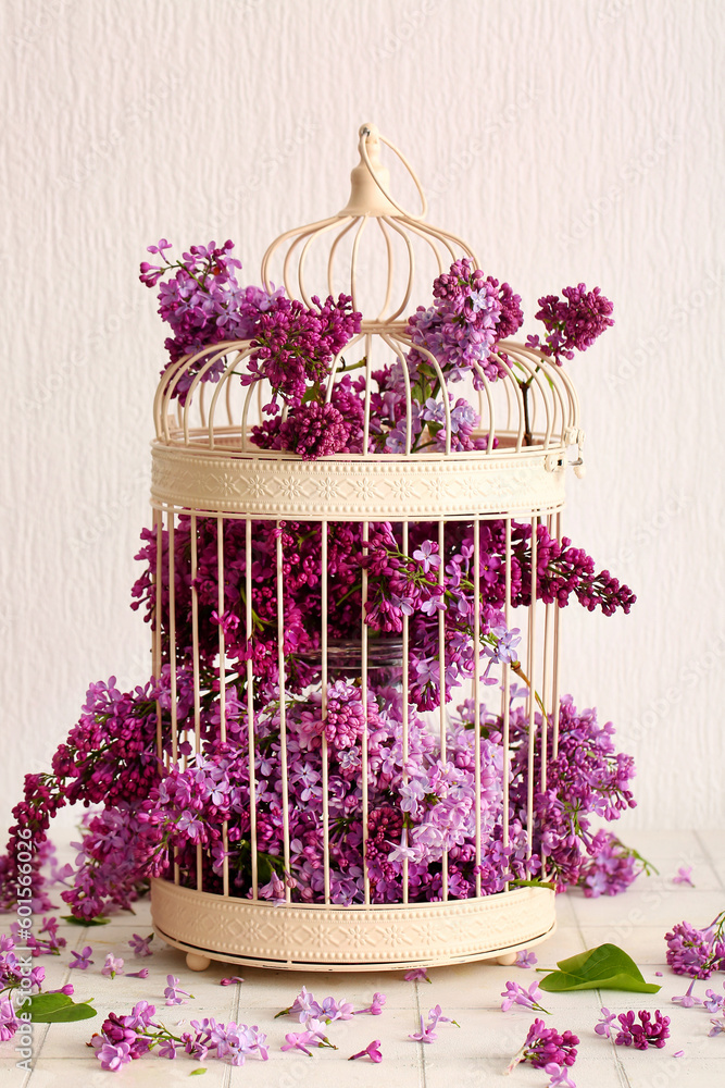 Birdcage with beautiful lilac flowers on light background