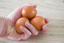 Hand Holding Three Eggs On Wooden Table