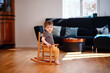© Иванна Емельянова - Little toddler boy sitting on wooden rocking chair in living room with dark sofa