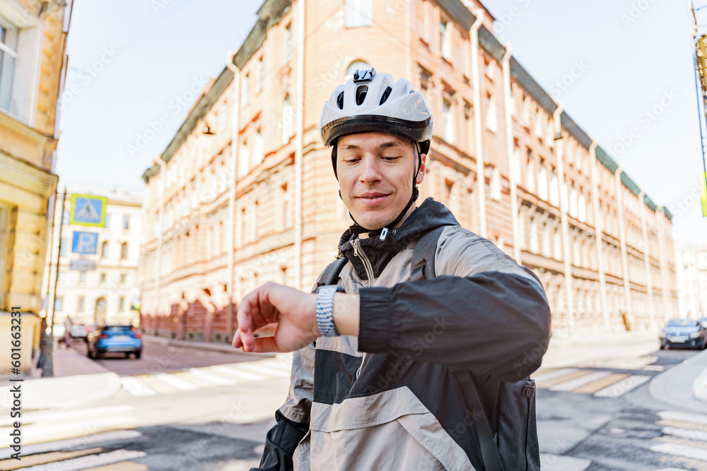 A young cyclist in a helmet uses a smartwatch on his hand, looks at the ...