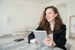 © muse studio - Using a tablet, a daily woman in a business suit is curly in the office, smiling and looking away.