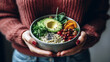 A bowl of healthy food: porridge, chia seeds, avocado, vegetables and greens in the hands of a woman. Close-up. Woman in sweater and jeans holding a bowl of healthy food, AI generated