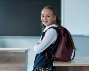 Wall Mural - Portrait of a caucasian schoolgirl with a backpack in the classroom on the background of the school board.
