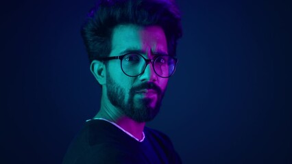 Indian man guy profile turning head looking camera serious developer coding internet technology hacker programmer Arabian male in glasses neon blue ultraviolet studio background high-tech cyberspace