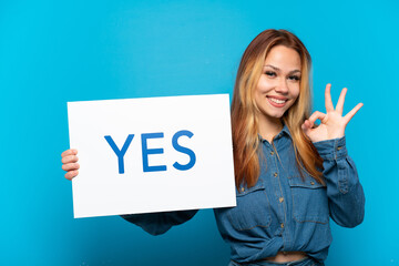 Teenager girl over isolated blue background holding a placard with text YES