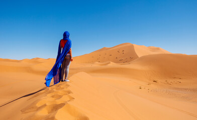 Wall Mural - Rear view of woman wearing waving blue turban in the desert- Sahara desert in Morocco