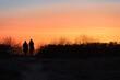 Die dunklen Silhouetten von 2 Personen beobachten den orangenen Sonnenuntergang am Strand von Rügen an der Ostsee. 