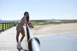 Beautiful young woman with long brown hair dressed in short skirt and shirt leaning on the railing of the wooden footbridge over the sea. In the background the atlantic ocean in conil in cadiz.