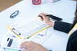 © ND STOCK - Close-up of woman's hand writing on spiral notepad lying on wooden desktop with various items