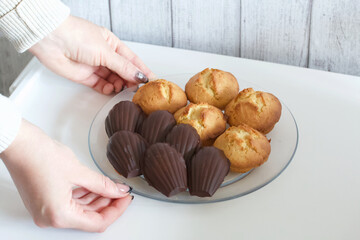 Wall Mural - A woman is holding a plate of homemade muffins and chocolate-covered Madeleine cookies.