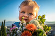 © J S - Cute Mother's Day card image of an adorable baby child holding a bouquet of colorful flowers as present on blue sky background with copy space, generative ai