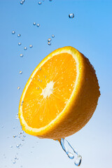 Poster - Water pours on half an orange on a blue background. Fresh tasty citrus fruit