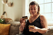 © Chanelle Malambo/peopleimages.com - Phone, credit card and woman on sofa online shopping, e commerce and fintech payment, loan or happy finance. Person on couch typing banking information on mobile app for home transaction and finance