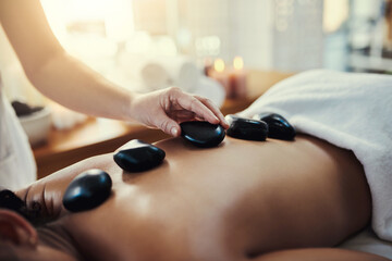 Wall Mural - Woman, hands and rocks for back massage at spa in beauty relaxation or skincare on bed. Hand of masseuse applying hot rock or stones on female for physical therapy, zen or skin treatment at resort