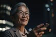 © InfiniteFlow - a senior chinese japanese businesswoman executive using mobile phone with background of modern office buildings at night Generative AI AIG18.