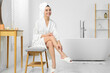 © New Africa - Beautiful happy woman in stylish bathrobe sitting on bench in bathroom