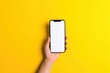 © diego - hand holding a phone with screen, hand holding a smart phone with blank screen isolated on a yellow colored background