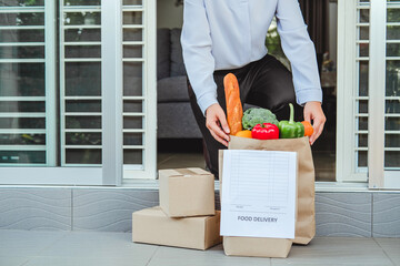 Wall Mural - Food Delivery concept. Asian woman hand accepting bag of food, fruit, vegetable delivery from professional deliveryman Postman and express grocery delivery.