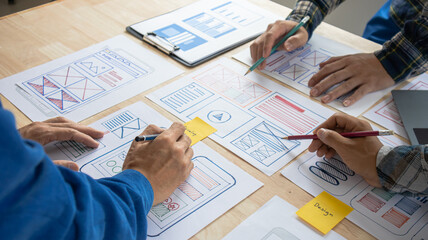 Close-up ux developers and ui designers use augmented reality to brainstorm on mobile app interface wireframe designs on modern office desks. Creative digital development office