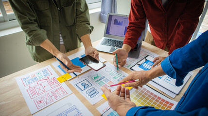 Close-up ux developers and ui designers use augmented reality to brainstorm on mobile app interface wireframe designs on modern office desks. Creative digital development office