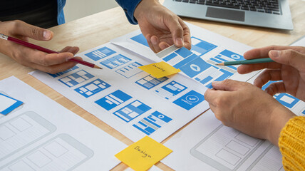 Close-up ux developers and ui designers use augmented reality to brainstorm on mobile app interface wireframe designs on modern office desks. Creative digital development office