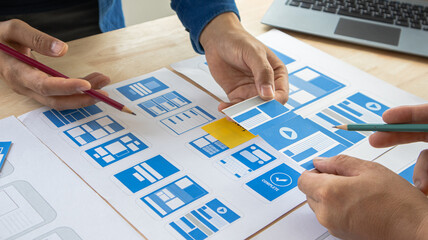Close-up ux developers and ui designers use augmented reality to brainstorm on mobile app interface wireframe designs on modern office desks. Creative digital development office