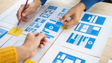 Close-up ux developers and ui designers use augmented reality to brainstorm on mobile app interface wireframe designs on modern office desks. Creative digital development office
