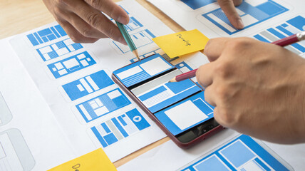 Close-up ux developers and ui designers use augmented reality to brainstorm on mobile app interface wireframe designs on modern office desks. Creative digital development office