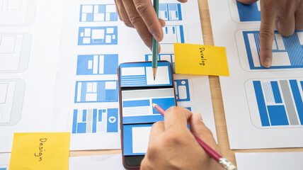 Close-up ux developers and ui designers use augmented reality to brainstorm on mobile app interface wireframe designs on modern office desks. Creative digital development office
