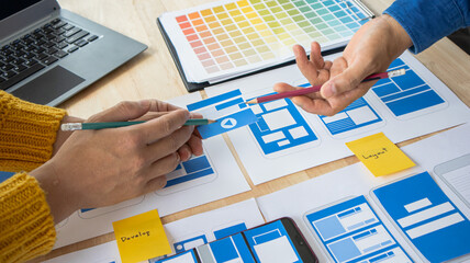 Close-up ux developers and ui designers use augmented reality to brainstorm on mobile app interface wireframe designs on modern office desks. Creative digital development office