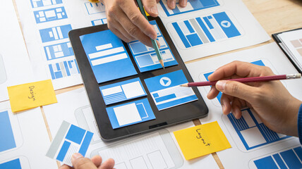 Close-up ux developers and ui designers use augmented reality to brainstorm on mobile app interface wireframe designs on modern office desks. Creative digital development office