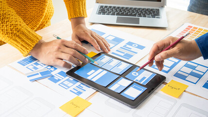 Close-up ux developers and ui designers use augmented reality to brainstorm on mobile app interface wireframe designs on modern office desks. Creative digital development office