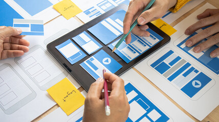 Close-up ux developers and ui designers use augmented reality to brainstorm on mobile app interface wireframe designs on modern office desks. Creative digital development office