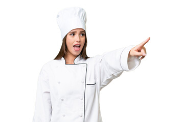 Young chef caucasian woman over isolated background pointing away